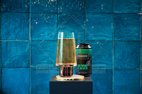 Tall flute with sparkling drink and can of lychee fizz styled against teal tile.