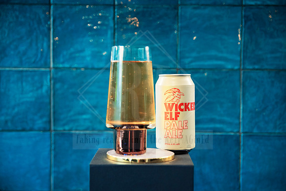 Tall flute with bubbles beside a can of beer on a gold pedestal.