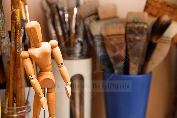 Close-up of wooden mannequin and paintbrushes in studio cup, styled detail image for Artwalk marketing material.