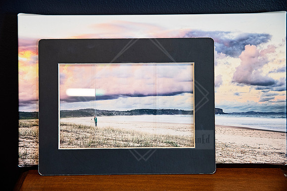 Mounted photo print displayed in a black frame with beach scene as backdrop.