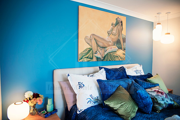 Styled bedroom with layered velvet cushions and blue feature wall adorned with nude artwork.