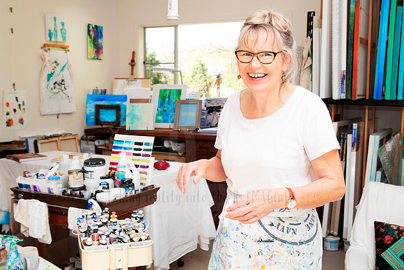 Smiling artist in light-filled studio surrounded by art supplies, captured for personal branding photography.