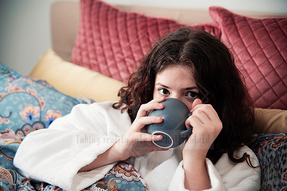Guest peeking over a mug while tucked into bed with a cheeky smile.