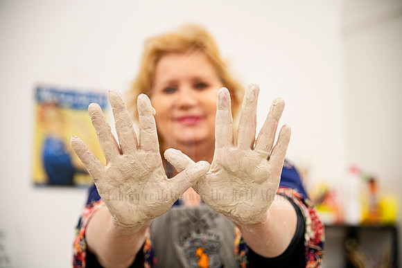 Artist holding up muddy hands with a smile after working clay, joyful moment captured for Artwalk promo.