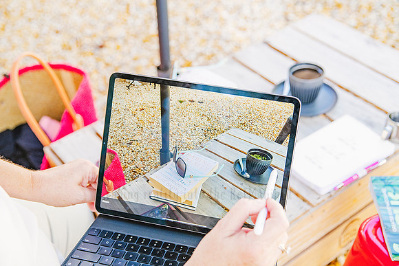 Laptop and coffee setup outdoors with reflection of umbrella and beach, lifestyle content for Bron Watson & Co.