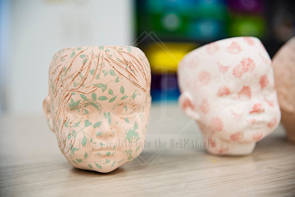 Close-up of ceramic head-shaped pots with delicate painted details, created for Artwalk artist showcase.