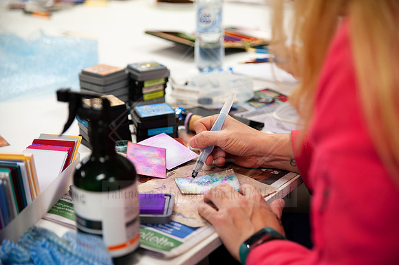Hands painting vibrant artwork during workshop, with art tools and branding materials in frame for visual content creation.