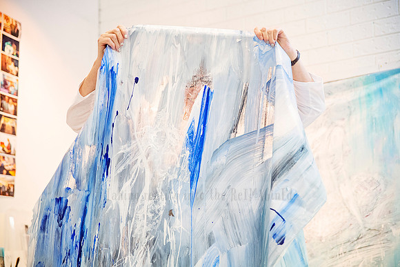 Artist holding up a large translucent textile piece with vivid blue and white paint streaks.