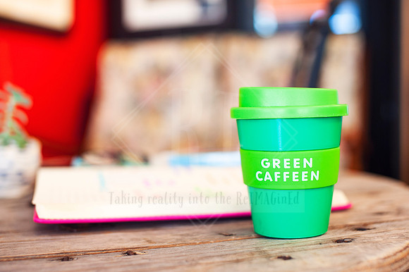 Flat lay of Green Caffeen reusable cup and journal in a café workspace, content created for eco-conscious branding.