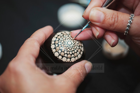 Hand-detail shot of artist applying tiny dots to a roundl object, photographed for creative business content.