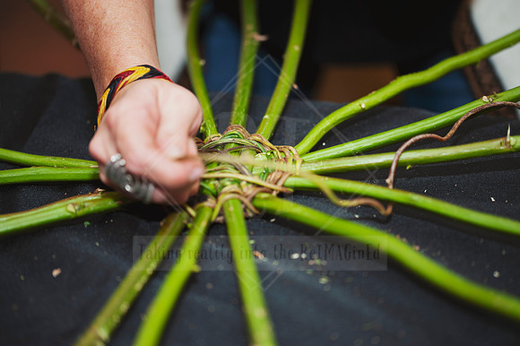 Artisan hands forming the base of a woven piece with reeds, photographed during a hands-on workshop.