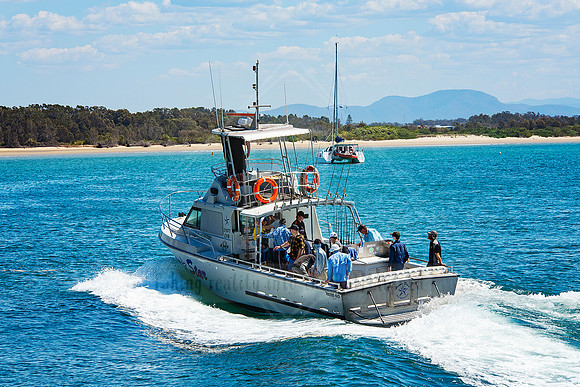 Angled view of fishing boat underway with visible crew and tourists enjoying the ride.