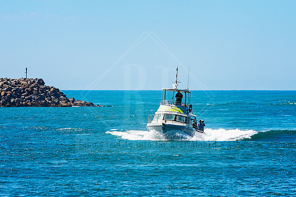 Fishing boat speeding past the breakwall under bright blue skies in Port Macquarie.