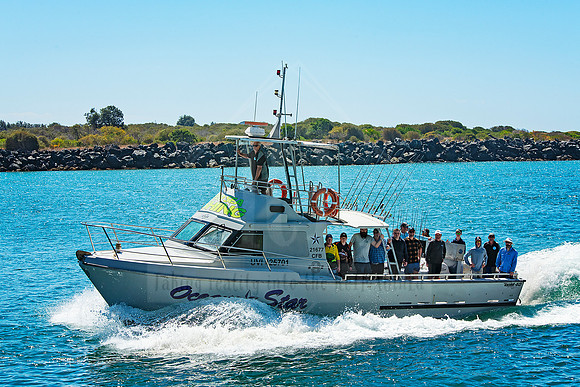 Fishing charter boat full of passengers cruising near the coast under a sunny sky.