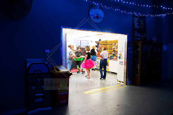 Entryway of Planet Skate lit with colourful neon, people entering under roller derby banner.