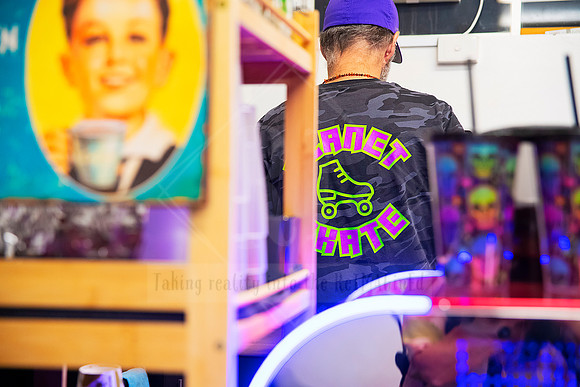 Back view of skater in branded 'Planet Skate' tee surrounded by bright neon lights.