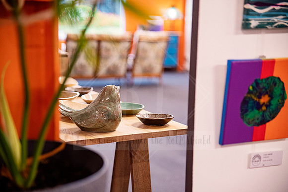 Artworks and ceramic decor on a timber plinth in a warmly lit gallery corner.