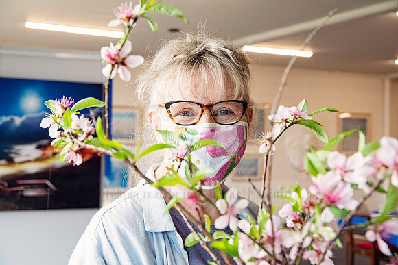 Smiling woman wearing glasses and mask holding pink blossom stems, captured at Yvonne Kiely Art event.