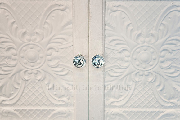 Pressed tin cupboard doors with vintage-style clear crystal knobs in soft lighting.