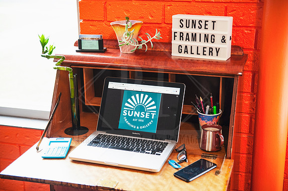 Laptop with Sunset Framing & Gallery logo set against vibrant orange wall, styled flat lay for digital business content.