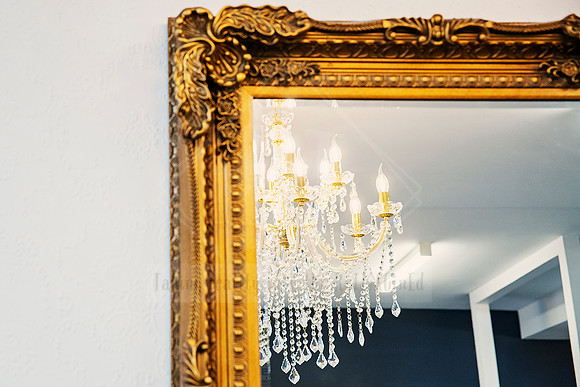 Close-up of intricate gold frame edge reflecting salon chandelier.
