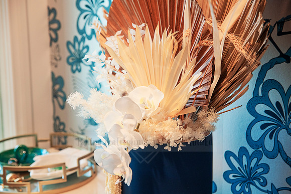 Blue and beige dried flower bouquet with shells and feathers in a tall vase.