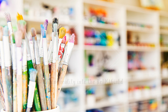 Pot of used paintbrushes with labelled handles in a bright studio space.