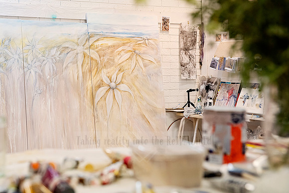 Artist studio with large mural in progress, blurred foreground of paints and brushes.
