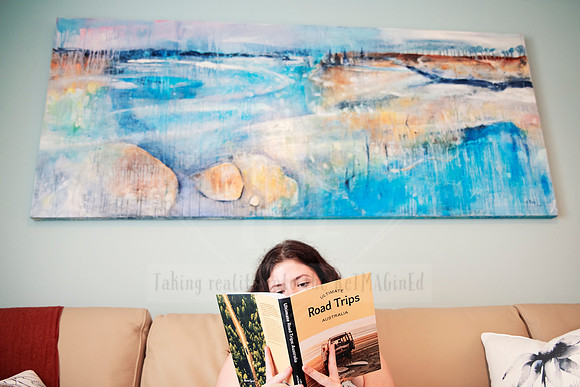Guest reading a travel book on a neutral-toned lounge under a coastal abstract painting.