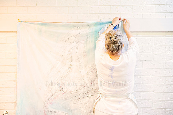 Back view of Yvonne pinning the top of her abstract artwork to the wall during installation.