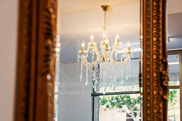 Salon chandelier reflected in a mirror, framed by antique gold trim.