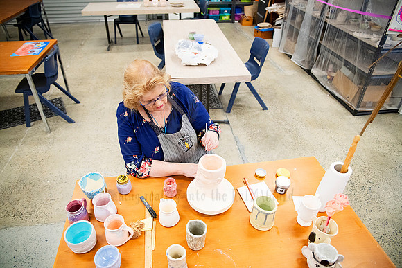 Aerial view of artist decorating ceramic pieces at a large table, captured as part of Artwalk’s creative workshop series.