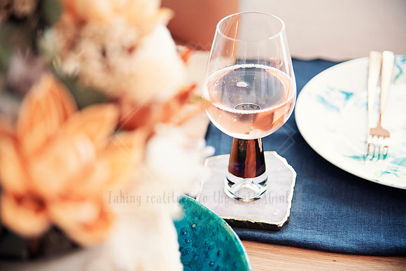 Glass of wine with dried florals blurred in foreground on table setting.