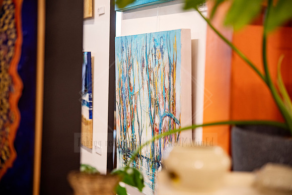 Gallery scene with artworks on display and potted greenery in the foreground.