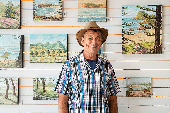 Portrait of artist standing before a wall of painted landscapes, photographed for Artwalk’s artist profile series.