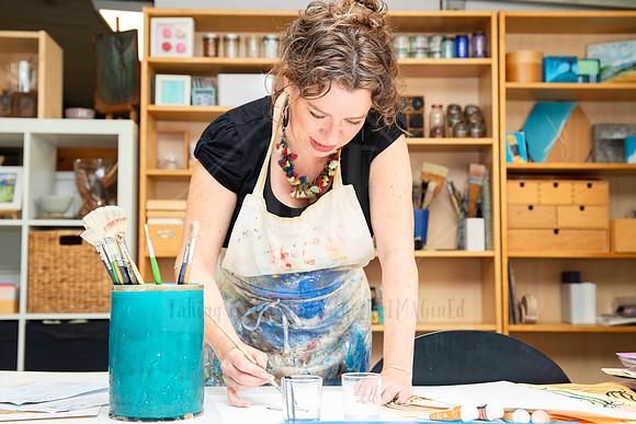 Artist in apron working over table with vibrant paints, captured mid-process for behind-the-scenes Artwalk storytelling.