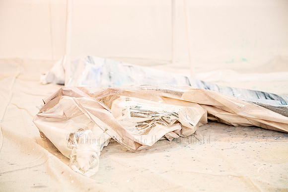 Canvas works partially folded on the studio floor, with textured, neutral-toned drop cloths.