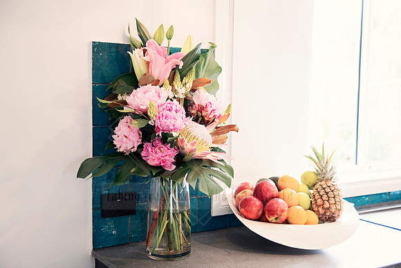 Fresh floral arrangement with fruit bowl and dark chopping board on kitchen counter.