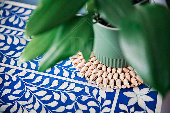 Green vase on blue floral tablecloth with scattered natural shell beads and leafy foliage.