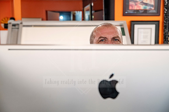 Man peeking over an iMac computer at the front counter of Sunset Framing & Gallery.