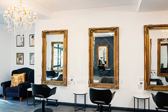 Salon seating area featuring black chairs, side tables, and gold mirrors under a chandelier.