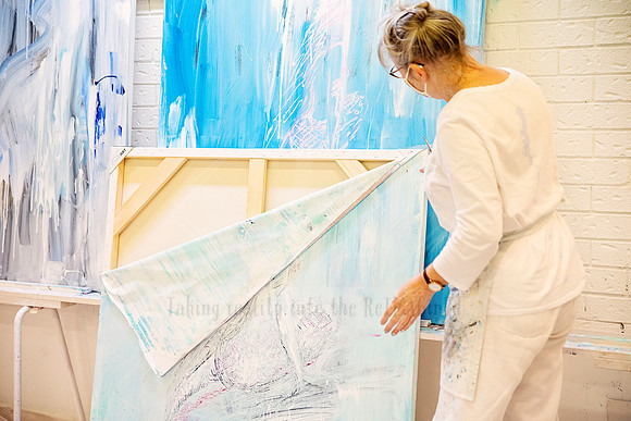 Artist lifting the corner of a large canvas with abstract lines and soft blue paint during installation.