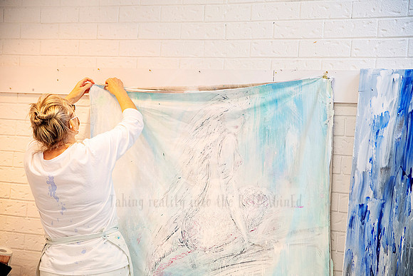 Woman hanging her expressive artwork on a white brick wall, mid-setup in the studio space.