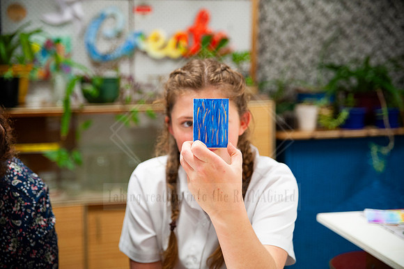 Young woman holding up blue painted artwork in creative studio, photographed for small business brand storytelling.