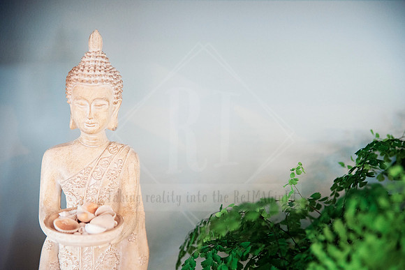 Carved Buddha statue holding a tealight bowl, surrounded by potted greenery.