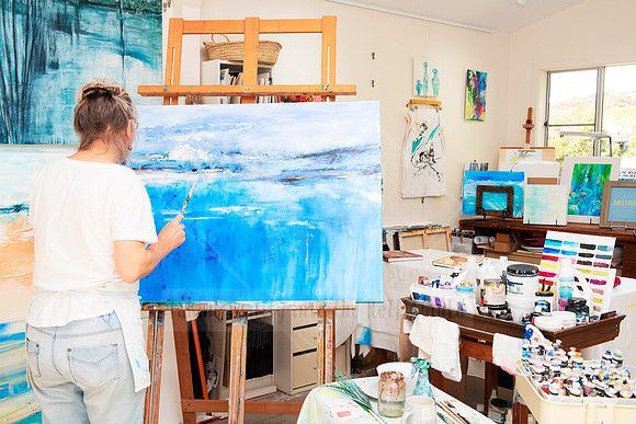Studio action shot of painter working on blue-toned canvas, part of business content series for Art Walk.