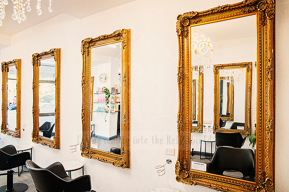 Row of vintage gold mirrors lined above salon chairs in a modern boutique setting.
