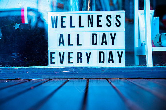 Lightbox sign spelling “WELLNESS ALL DAY EVERY DAY” on blue-toned surface, styled for Bron Watson & Co branding.