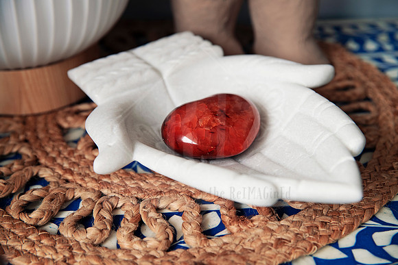 Flat lay of white ceramic dish with red crystal on a woven placemat and blue patterned cloth.