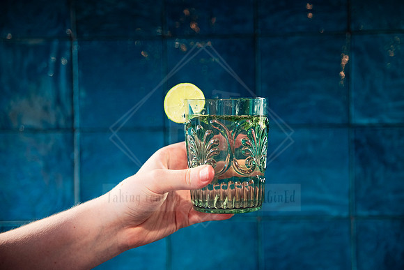 Green etched glass with a lime garnish held up in front of a teal feature wall.